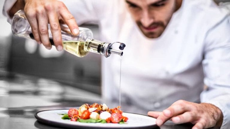 A photo of a chef pouring oil over a salad