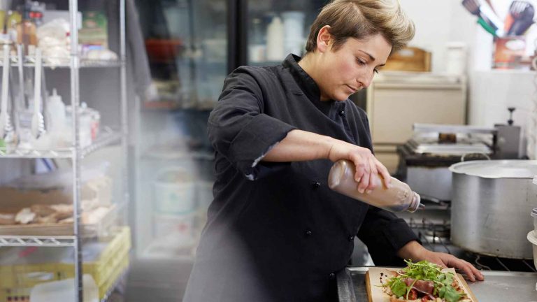 A female chef dressing a dish in the kitchen